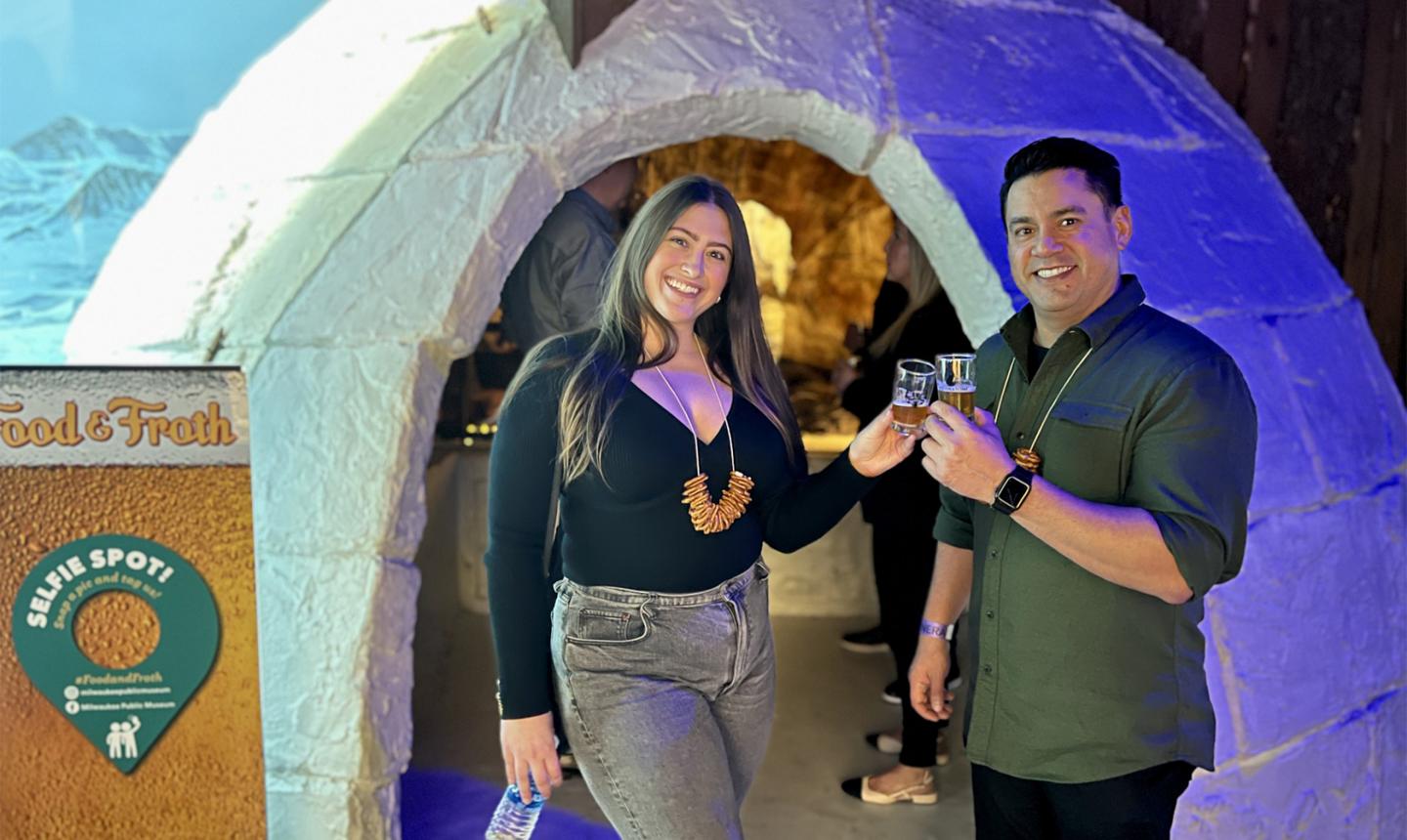 Couple standing in front of igloo while holding glasses of beer